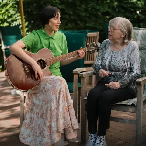 Therapeutin spielt einer Bewohnerin auf der Terrasse Gitarre vor