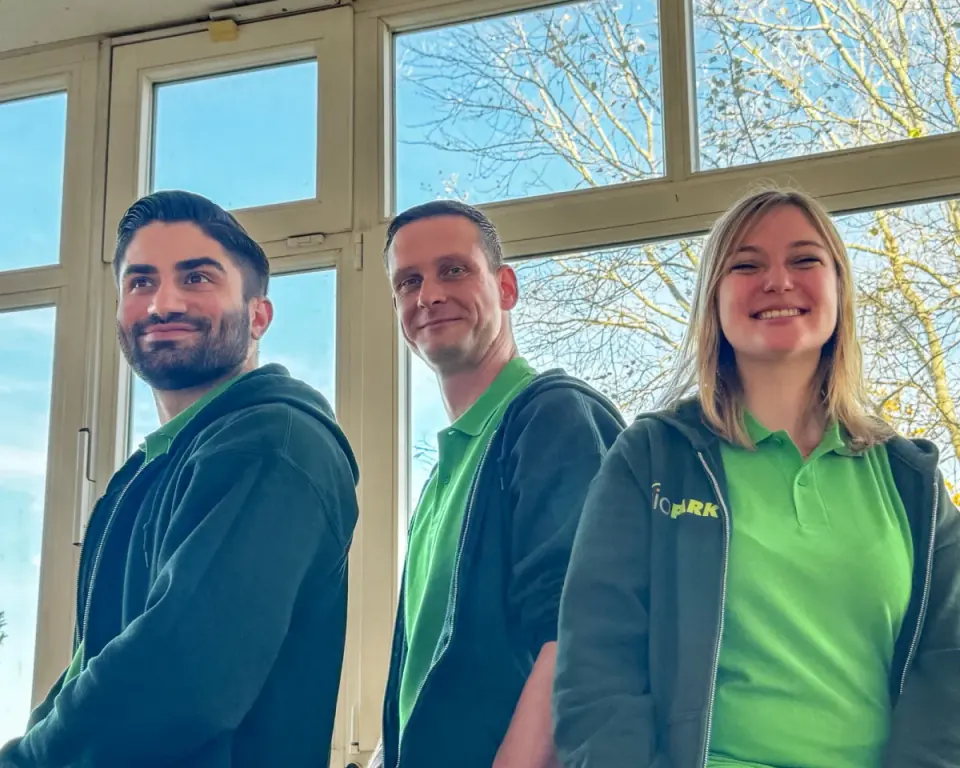 Drei Kolleginnen und Kollegen aus dem Team der Pflegeeinrichtungen in Dienstkleidung vor einem Fenster